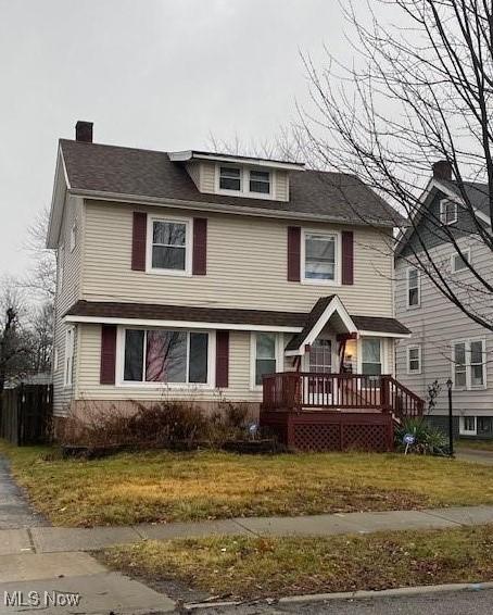 traditional style home featuring a chimney, a front yard, and a wooden deck