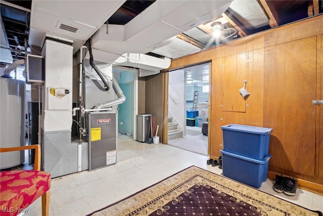 finished basement with tile patterned floors, visible vents, water heater, stairway, and heating unit