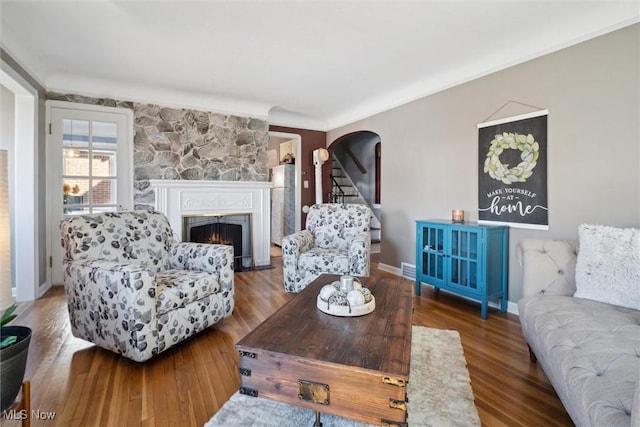 living room with baseboards, a lit fireplace, arched walkways, and wood finished floors