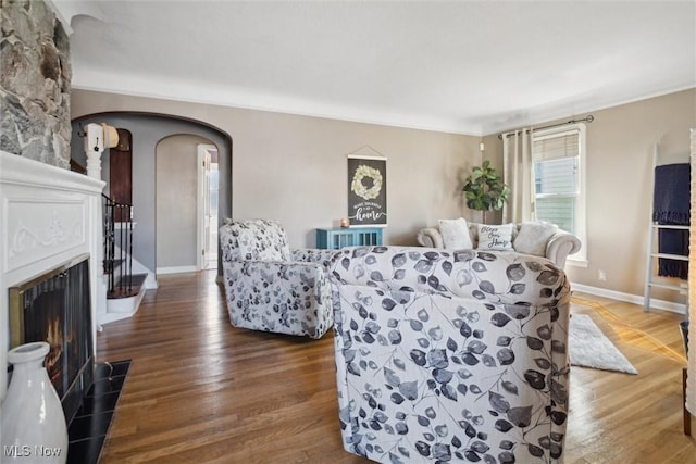 living room featuring a fireplace with flush hearth, arched walkways, baseboards, and wood finished floors