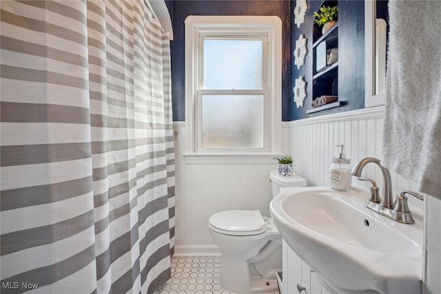 full bath with curtained shower, toilet, vanity, wainscoting, and tile patterned floors