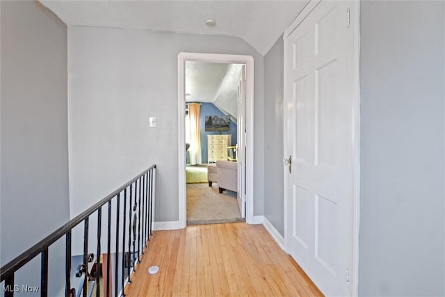 corridor featuring lofted ceiling, light wood finished floors, and baseboards