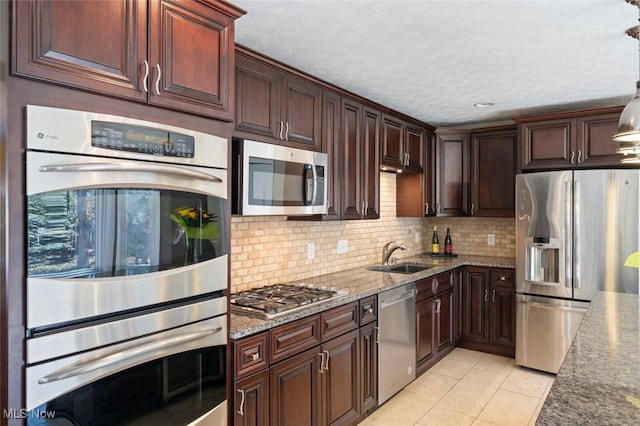 kitchen featuring appliances with stainless steel finishes, a sink, stone counters, backsplash, and light tile patterned flooring