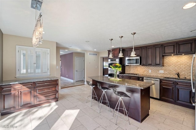 kitchen featuring stainless steel appliances, a breakfast bar, a kitchen island, tasteful backsplash, and dark stone countertops