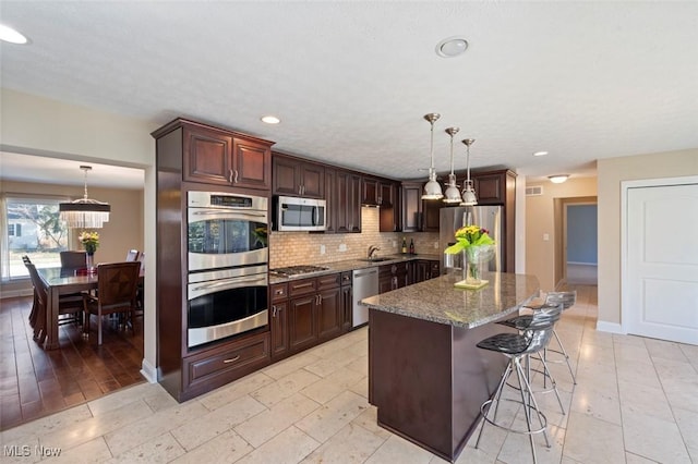 kitchen featuring stone counters, backsplash, appliances with stainless steel finishes, a sink, and a kitchen island