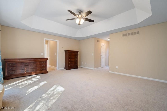 unfurnished bedroom featuring a tray ceiling, visible vents, light carpet, ceiling fan, and baseboards