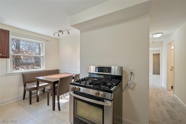 kitchen featuring light carpet, track lighting, stainless steel range with gas cooktop, and baseboards