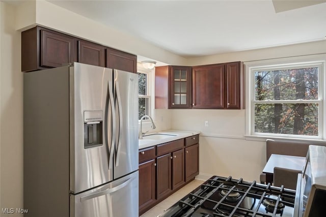 kitchen with light countertops, glass insert cabinets, a sink, dark brown cabinets, and stainless steel fridge with ice dispenser