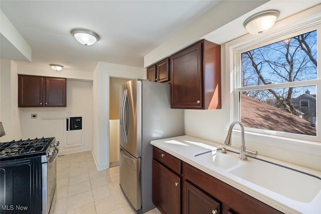 kitchen featuring light countertops, appliances with stainless steel finishes, a sink, dark brown cabinets, and baseboards