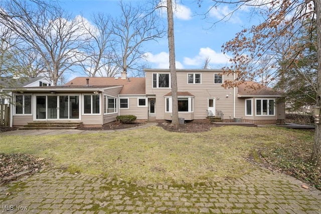 back of property featuring entry steps, a lawn, a chimney, and a sunroom