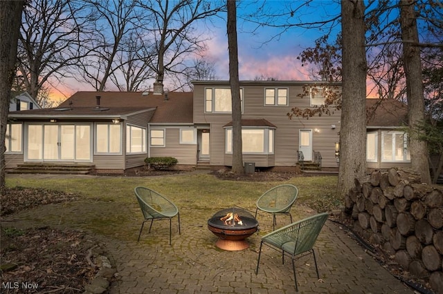 back of house at dusk featuring entry steps, a patio, an outdoor fire pit, and a chimney