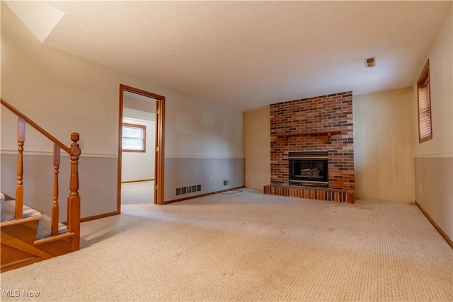 unfurnished living room featuring carpet floors, stairs, visible vents, and a fireplace