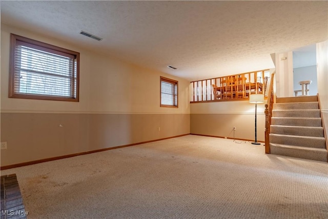 empty room with baseboards, visible vents, stairway, a textured ceiling, and carpet floors