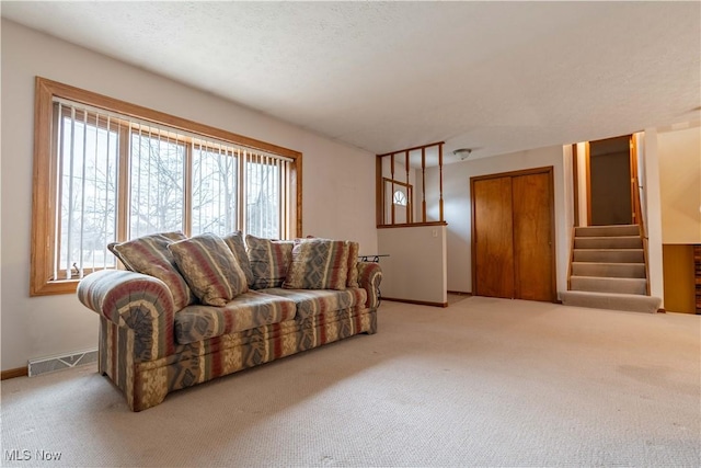 carpeted living room with stairway, baseboards, visible vents, and a textured ceiling