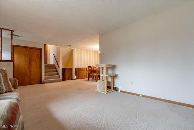 living area with carpet, visible vents, baseboards, and stairs