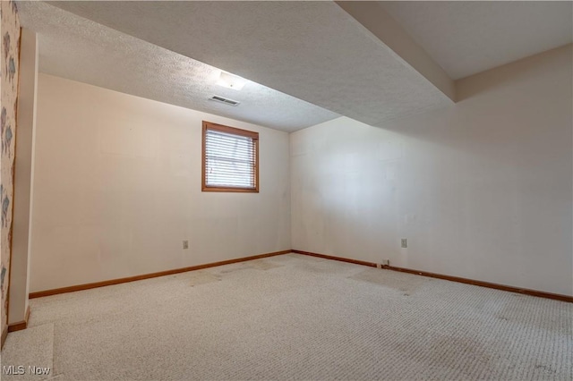 spare room featuring carpet, visible vents, baseboards, and a textured ceiling