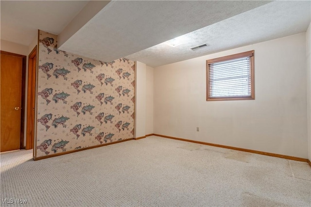 carpeted spare room featuring visible vents, a textured ceiling, baseboards, and wallpapered walls