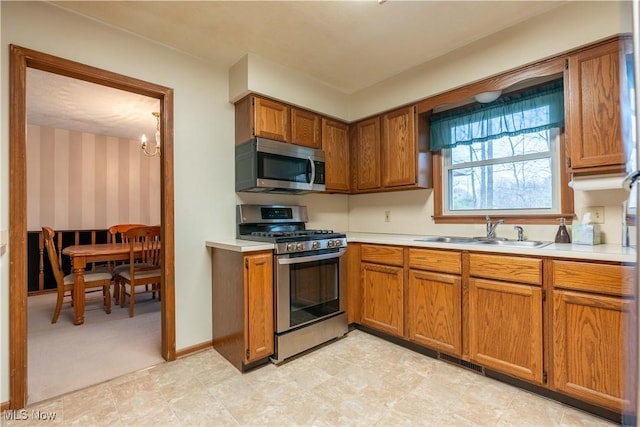 kitchen featuring appliances with stainless steel finishes, light countertops, brown cabinets, and a sink