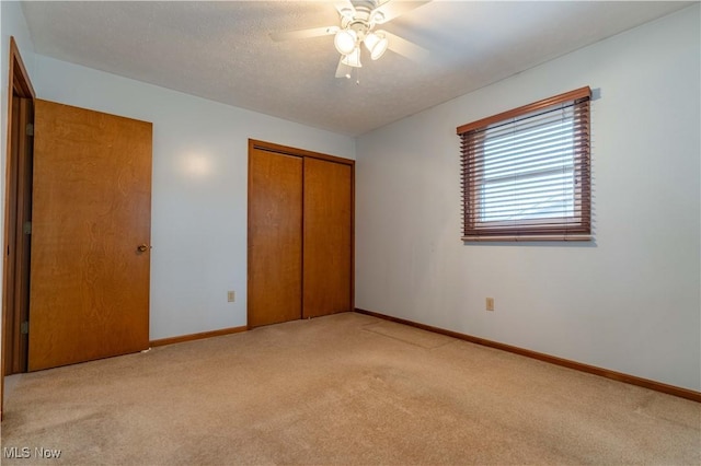 unfurnished bedroom featuring light carpet, a ceiling fan, baseboards, and a closet