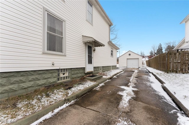 view of snowy exterior featuring aphalt driveway, an outbuilding, entry steps, fence, and a garage