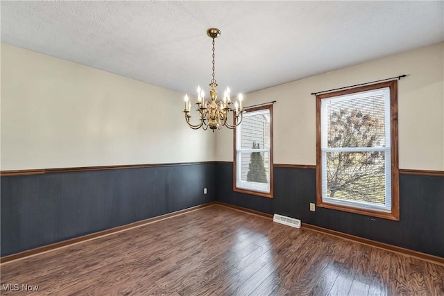 empty room featuring visible vents, a wainscoted wall, wood finished floors, a textured ceiling, and a notable chandelier