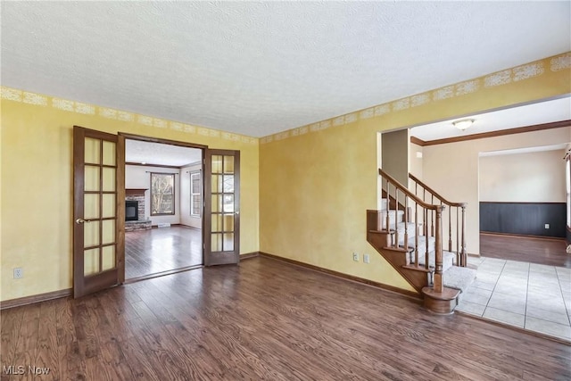 empty room featuring a textured ceiling, wood finished floors, stairs, french doors, and a glass covered fireplace