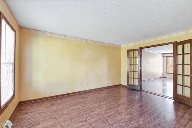 unfurnished room with a textured ceiling, baseboards, wood finished floors, and french doors