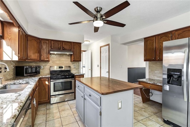 kitchen featuring a center island, light tile patterned floors, stainless steel appliances, a sink, and under cabinet range hood