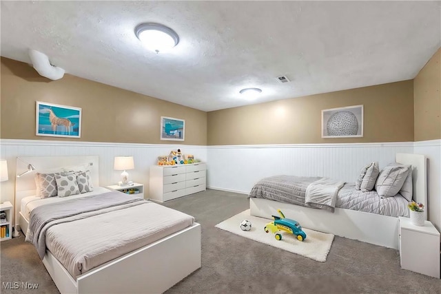 carpeted bedroom featuring a wainscoted wall and visible vents