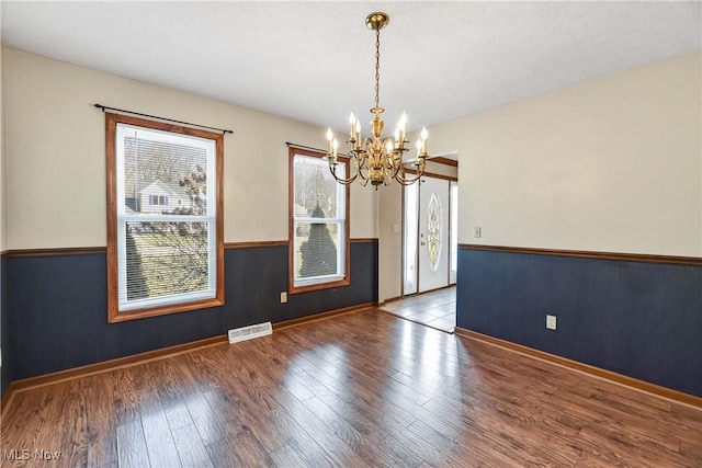 unfurnished room with a wainscoted wall, visible vents, a notable chandelier, and wood finished floors