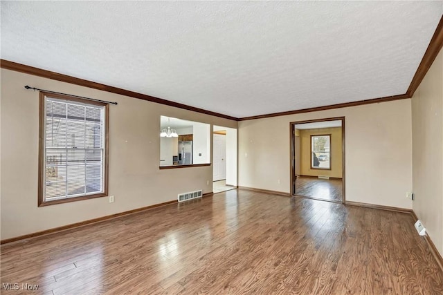 unfurnished room featuring a wealth of natural light, a textured ceiling, visible vents, and wood finished floors