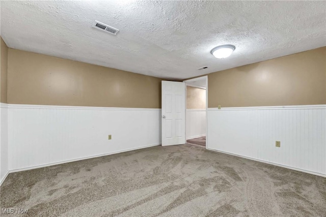 carpeted spare room featuring wainscoting, visible vents, and a textured ceiling