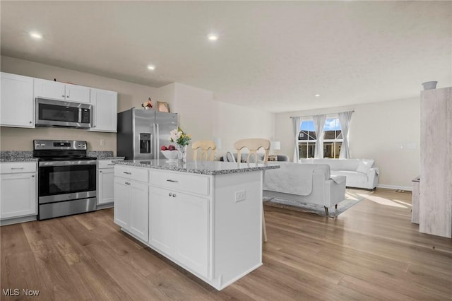 kitchen with stainless steel appliances, light stone counters, white cabinets, and light wood-style floors