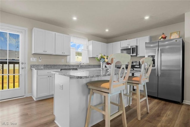 kitchen with a center island, a breakfast bar area, appliances with stainless steel finishes, white cabinetry, and wood finished floors