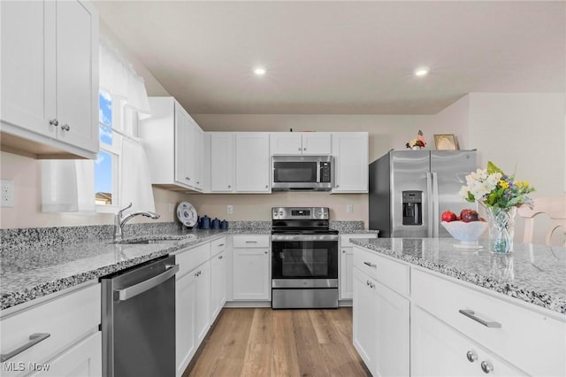 kitchen featuring stainless steel appliances, a sink, white cabinetry, light wood-type flooring, and light stone countertops