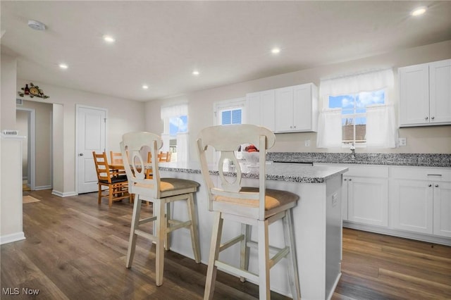 kitchen with a kitchen island, a kitchen breakfast bar, dark wood-style flooring, white cabinetry, and recessed lighting