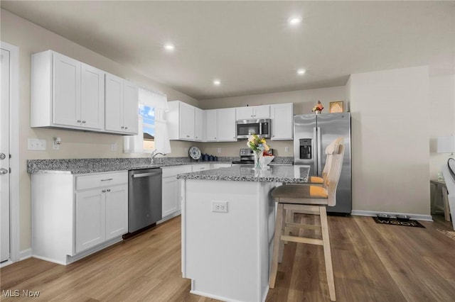 kitchen with white cabinetry, appliances with stainless steel finishes, wood finished floors, and a center island