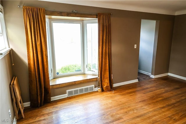 empty room with baseboards, visible vents, and wood finished floors