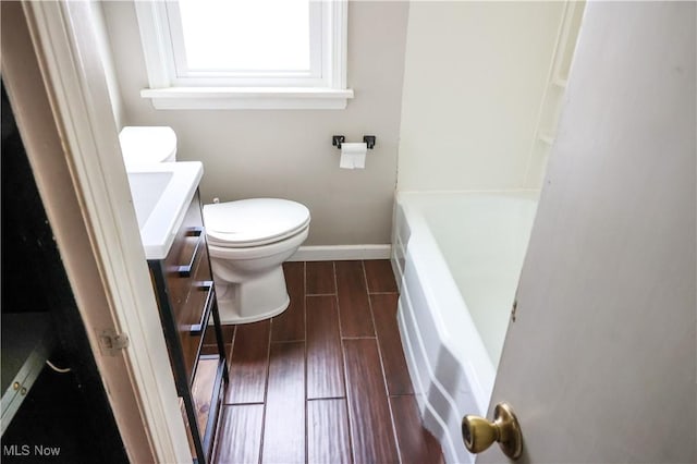 bathroom featuring baseboards, toilet, a bathing tub, vanity, and wood finish floors