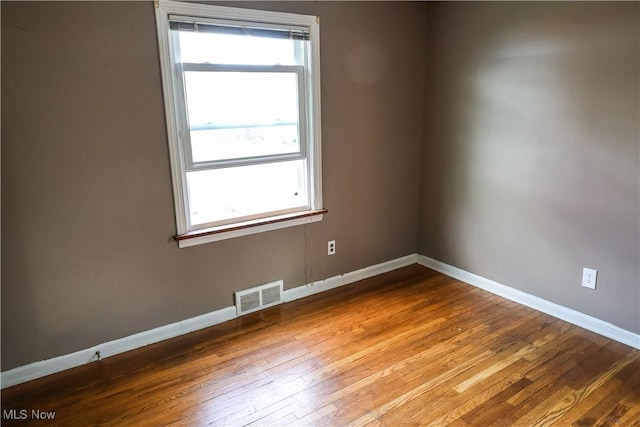 empty room with hardwood / wood-style flooring, baseboards, and visible vents