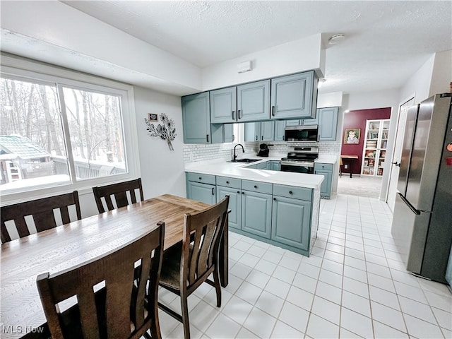 kitchen with appliances with stainless steel finishes, a peninsula, a sink, light countertops, and backsplash