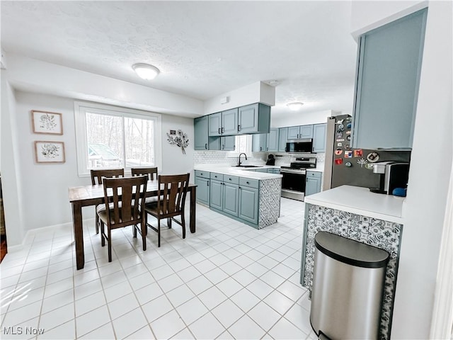 kitchen with gray cabinetry, a sink, light countertops, appliances with stainless steel finishes, and decorative backsplash