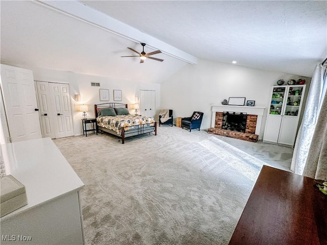 bedroom with visible vents, light colored carpet, lofted ceiling with beams, a ceiling fan, and a brick fireplace