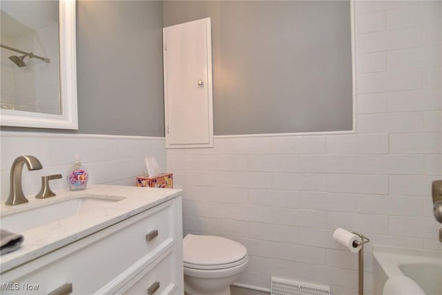 bathroom with visible vents, toilet, a wainscoted wall, vanity, and tile walls