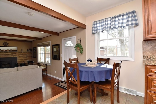 dining space with beam ceiling, visible vents, a brick fireplace, wood finished floors, and baseboards