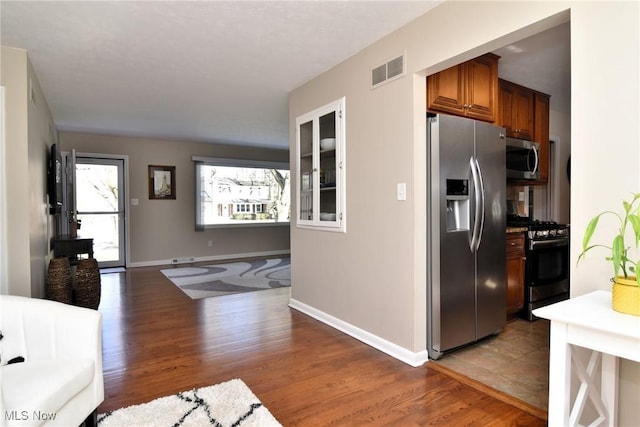 kitchen featuring appliances with stainless steel finishes, light wood-type flooring, brown cabinets, and baseboards