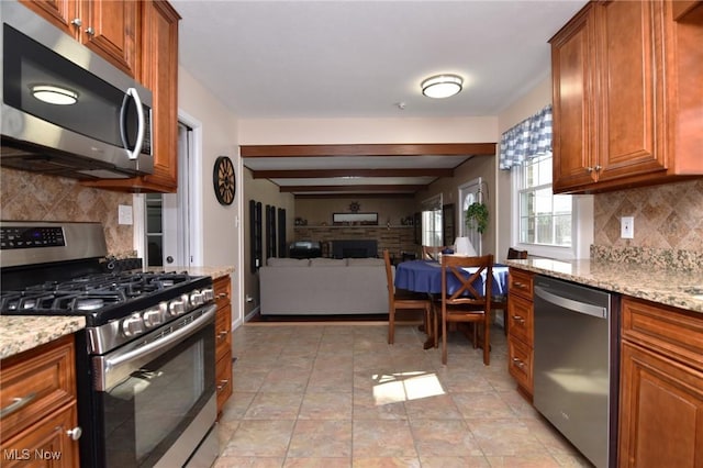 kitchen with light stone countertops, open floor plan, appliances with stainless steel finishes, brown cabinets, and decorative backsplash