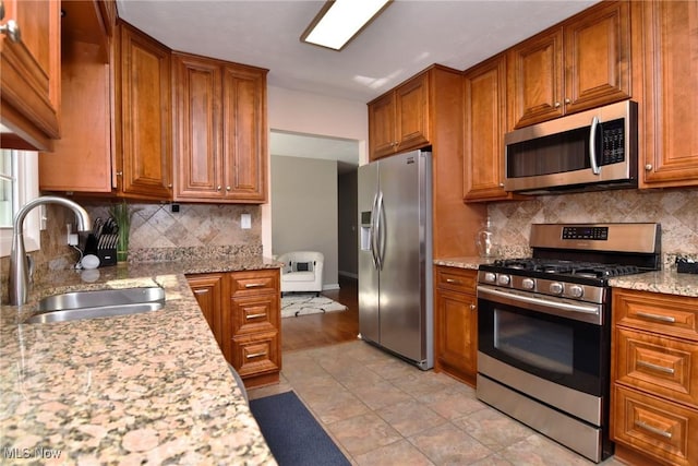 kitchen with decorative backsplash, appliances with stainless steel finishes, brown cabinetry, and a sink