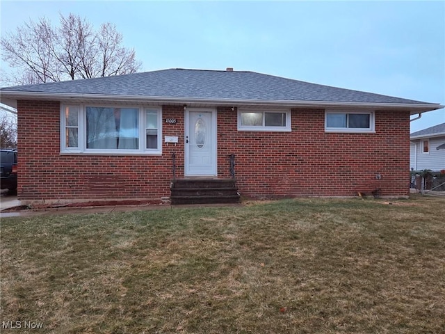 view of front facade featuring roof with shingles, a front lawn, and brick siding