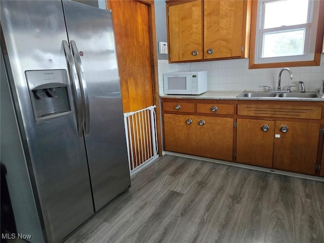 kitchen with brown cabinets, stainless steel refrigerator with ice dispenser, light countertops, white microwave, and a sink